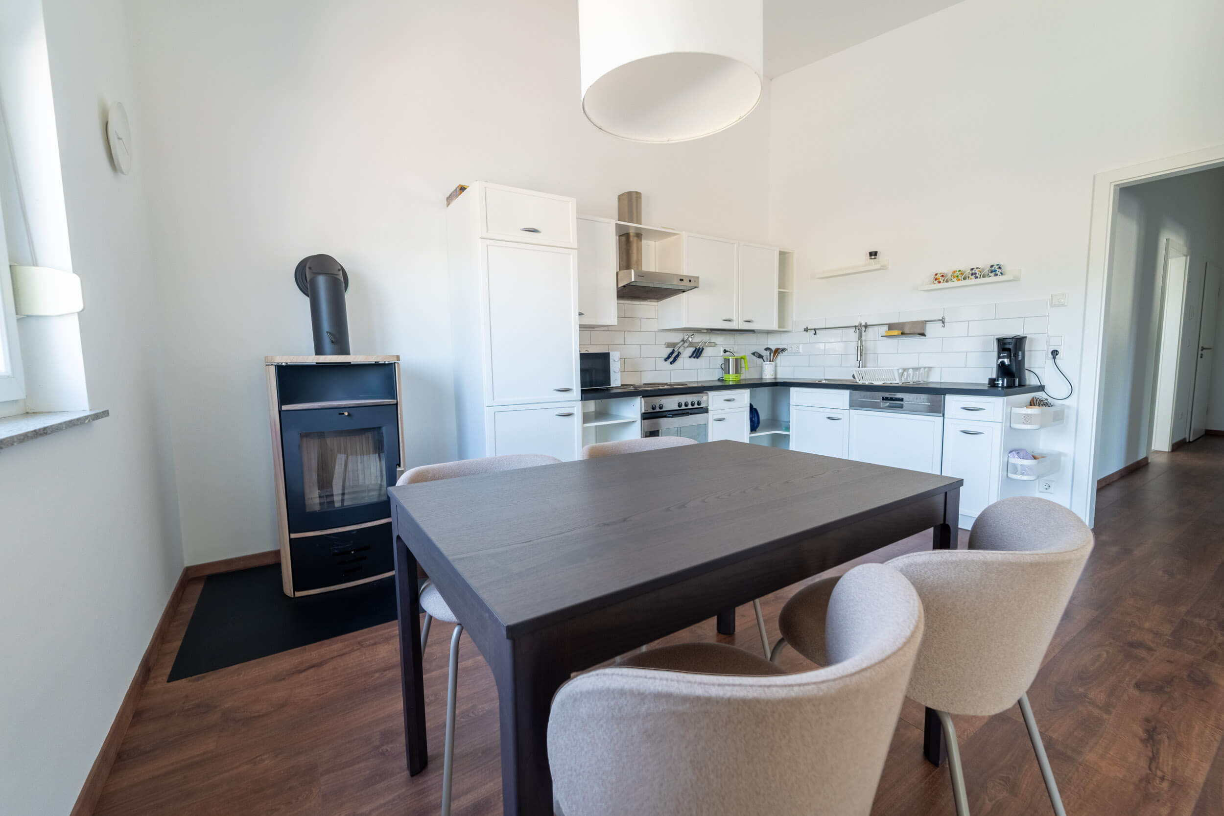 Offener Wohn- und Essbereich mit vier Stühlen vor einem Kamin und offener Küche.