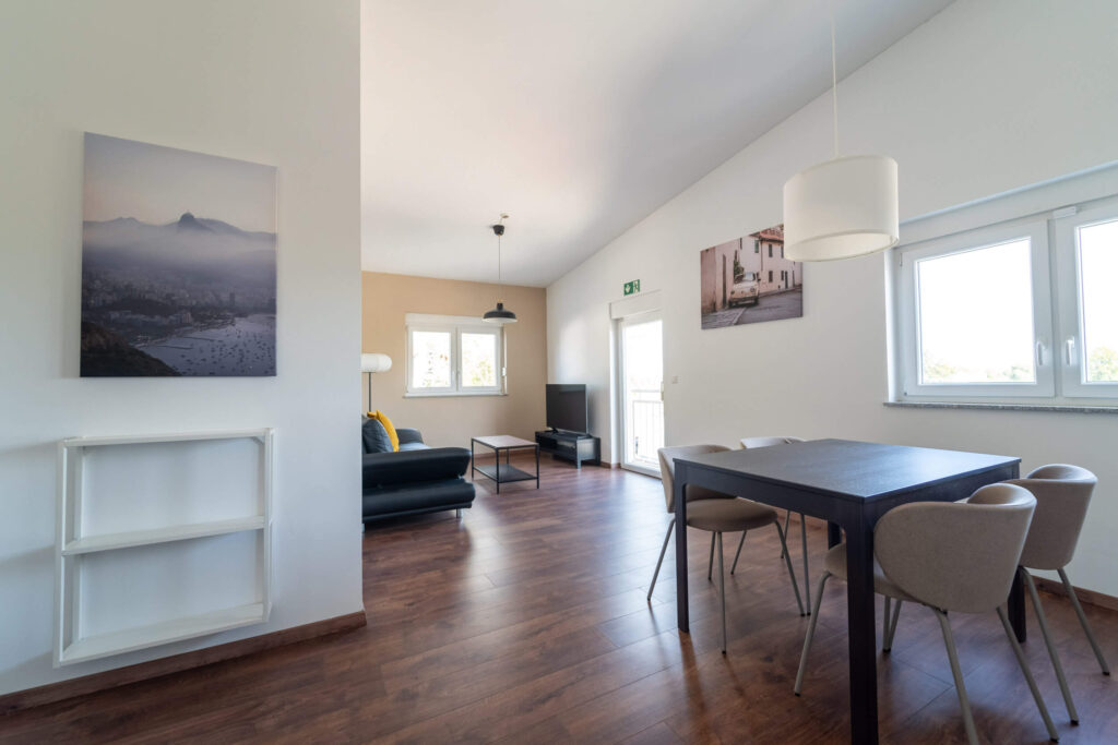 Offener Wohn- und Essbereich mit vier Stühlen, einer Couch mit Couchtisch sowie einer TV-Bank mit Fernseher.